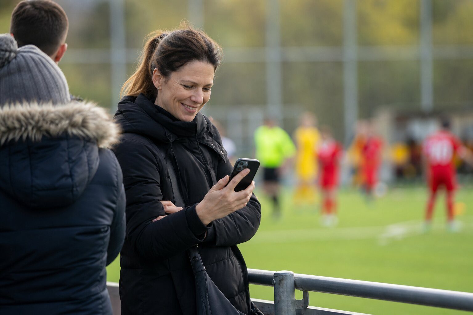 Mutter sieht am Spielfeldrand die Bilder ihres Sohnes auf dem Handy
